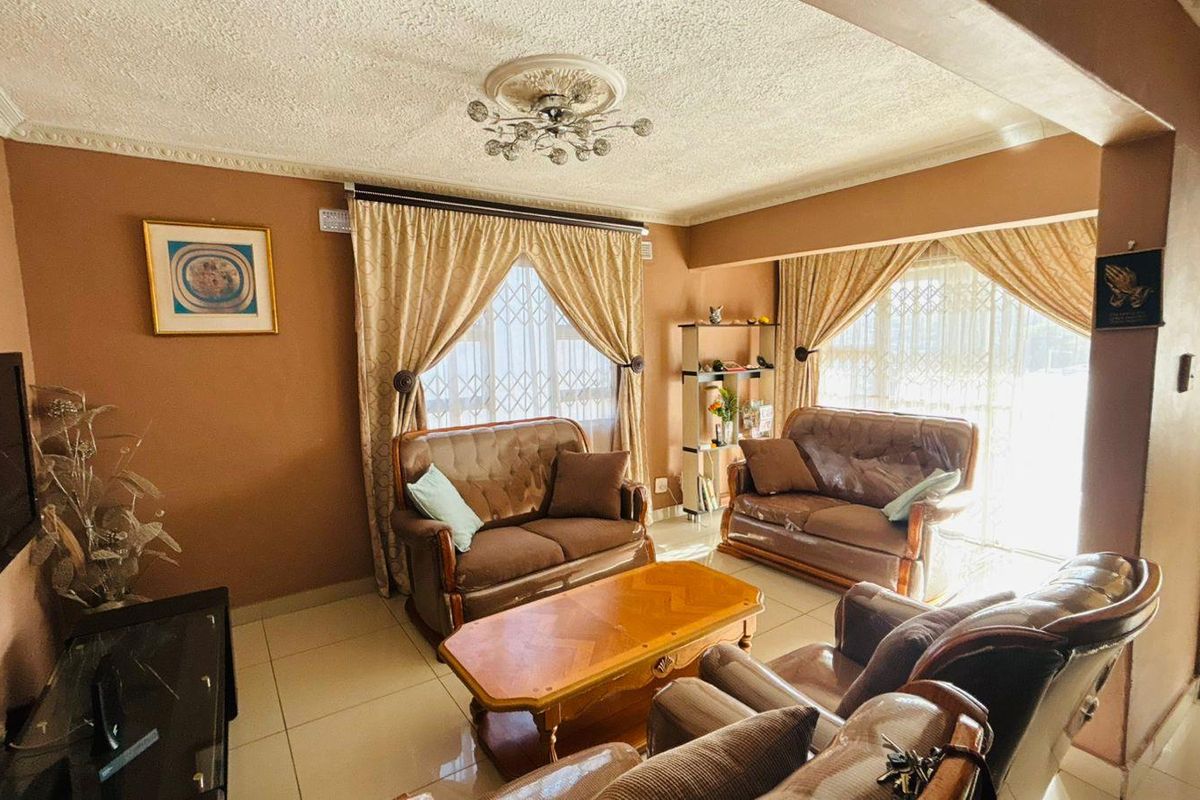 A comfortable living room featuring tiled flooring, decorative ceiling rose with light fixture, and large windows with security gates.