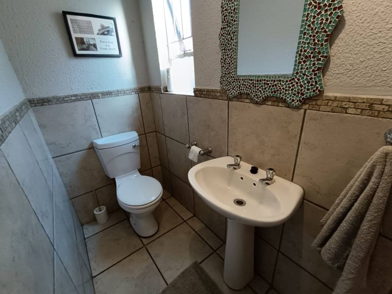 A compact guest bathroom featuring a pedestal basin, toilet, and neutral wall and floor tiling.