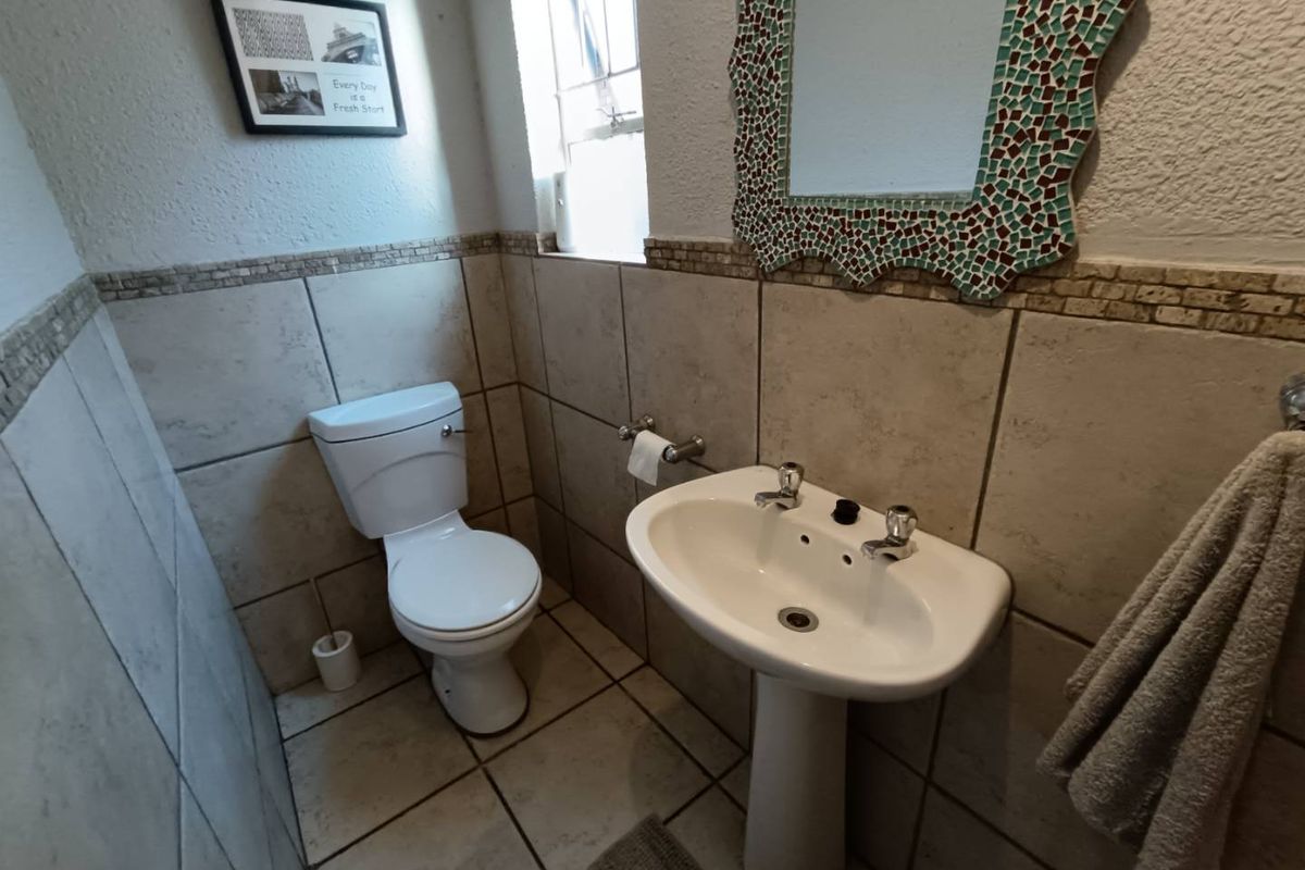 A compact guest bathroom featuring a pedestal basin, toilet, and neutral wall and floor tiling.