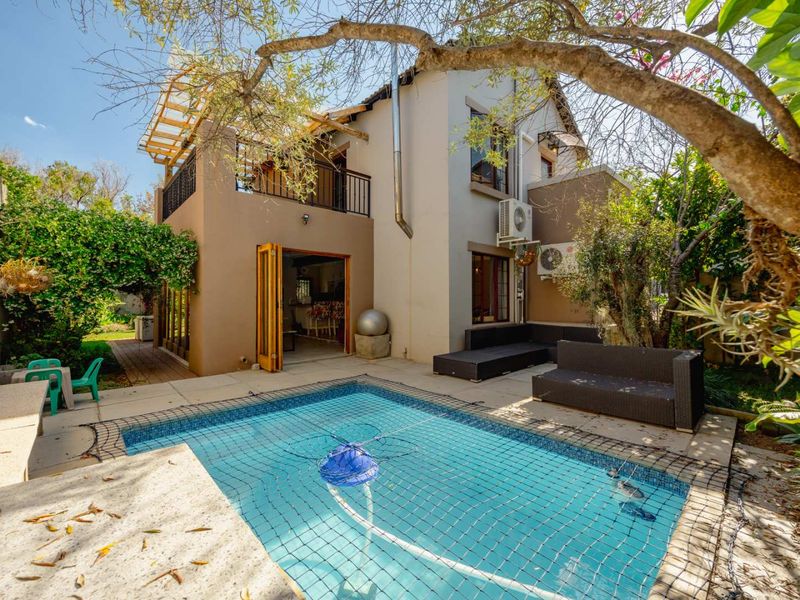 A private outdoor pool area featuring a safety net, paved patio space, and direct access to the home via bi-fold doors and an upper balcony.