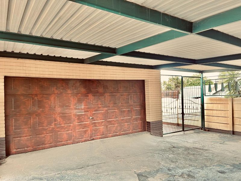 A covered carport area featuring a concrete driveway, a steel garage door, and secure wrought iron gate access.