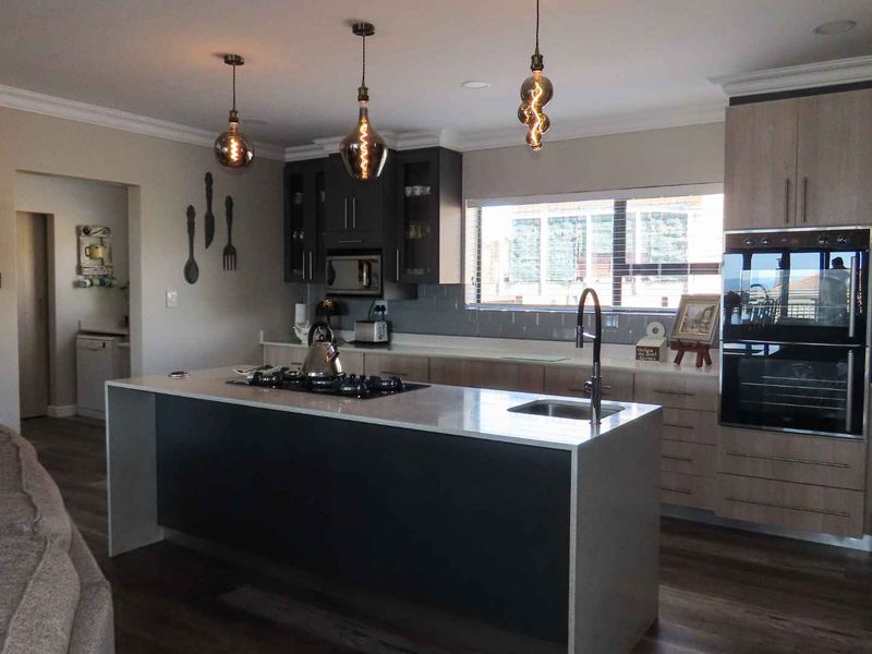 Modern open-plan kitchen featuring a central island with gas hob, stone countertops, built-in oven, and contemporary cabinetry with stylish pendant lighting.