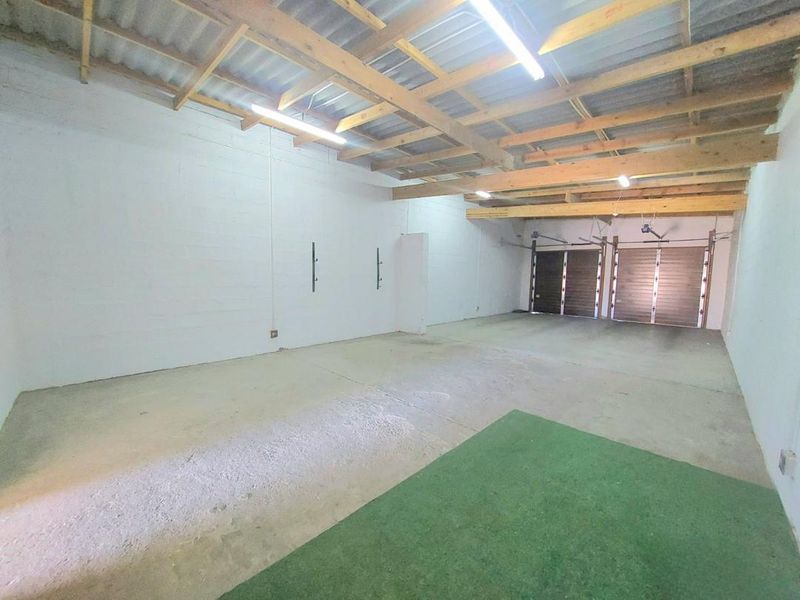 Spacious double garage featuring exposed timber roof trusses, fluorescent lighting, and concrete flooring, offering a versatile utility or storage space.