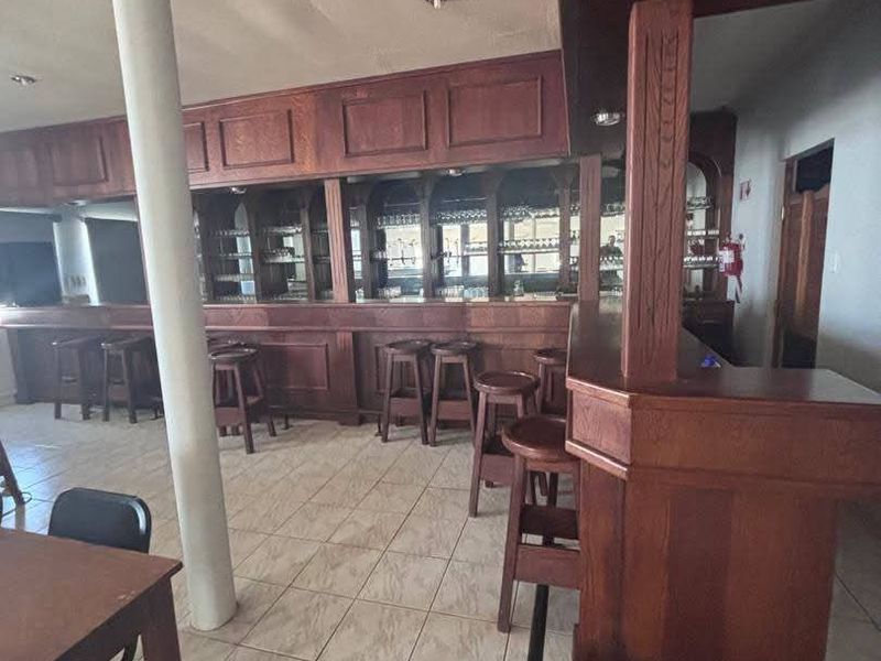 A spacious bar area featuring a large built-in wooden bar counter, back bar shelving, and tiled flooring, suitable for hospitality or entertainment use.
