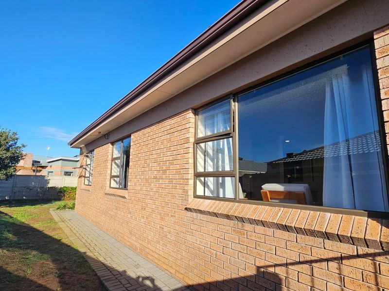 A view of the rear exterior facade featuring face brick construction, aluminium window frames, and a paved walkway along the side of the house.