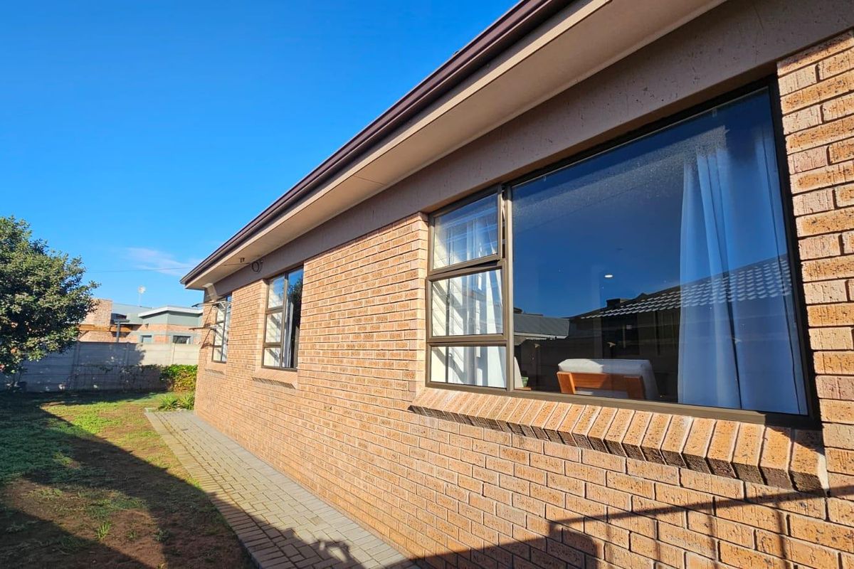 A view of the rear exterior facade featuring face brick construction, aluminium window frames, and a paved walkway along the side of the house.