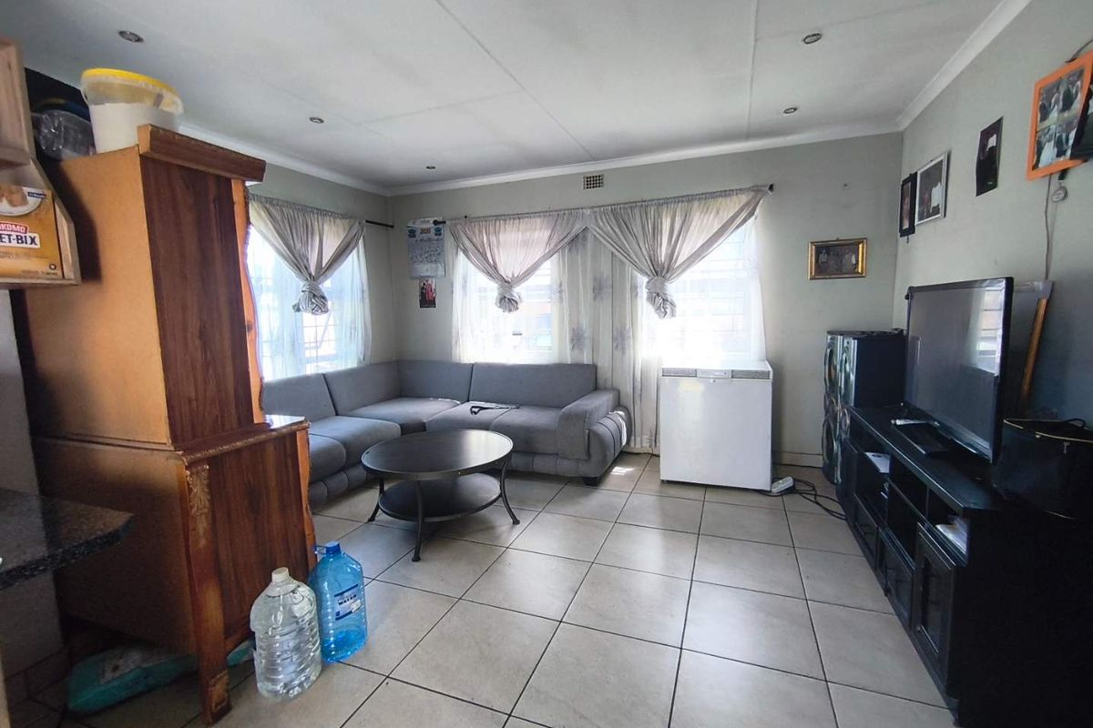 A spacious living room featuring neutral floor tiles, recessed ceiling lighting, and large windows that provide ample natural light.