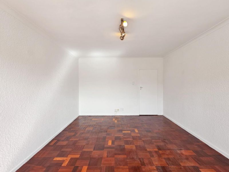 An empty living room featuring traditional parquet flooring, white walls, and a modern ceiling-mounted spotlight fixture.