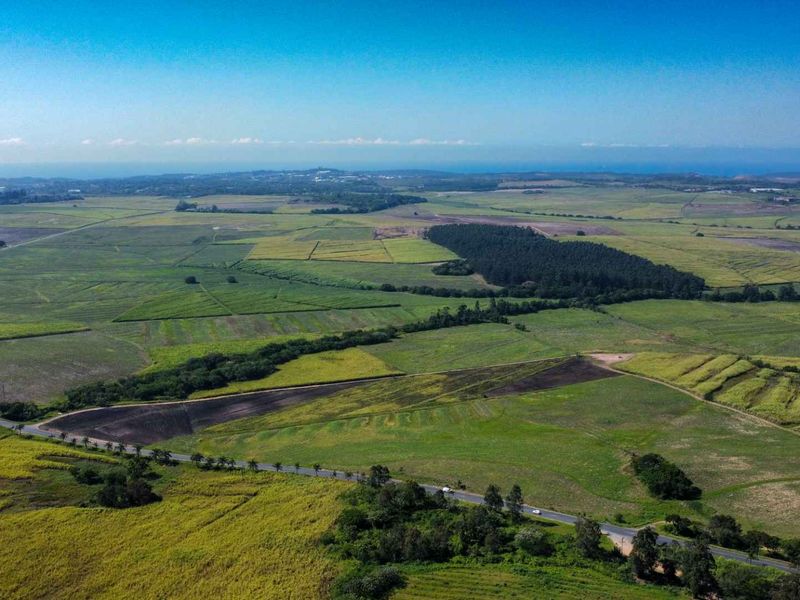 An expansive aerial view of the farm property, showcasing vast agricultural fields, surrounding woodland, and a bordering paved road.