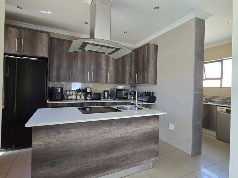Modern kitchen featuring dark wood-grain cabinetry, a central island with a built-in hob and sink, stone countertops, and integrated extractor fan.