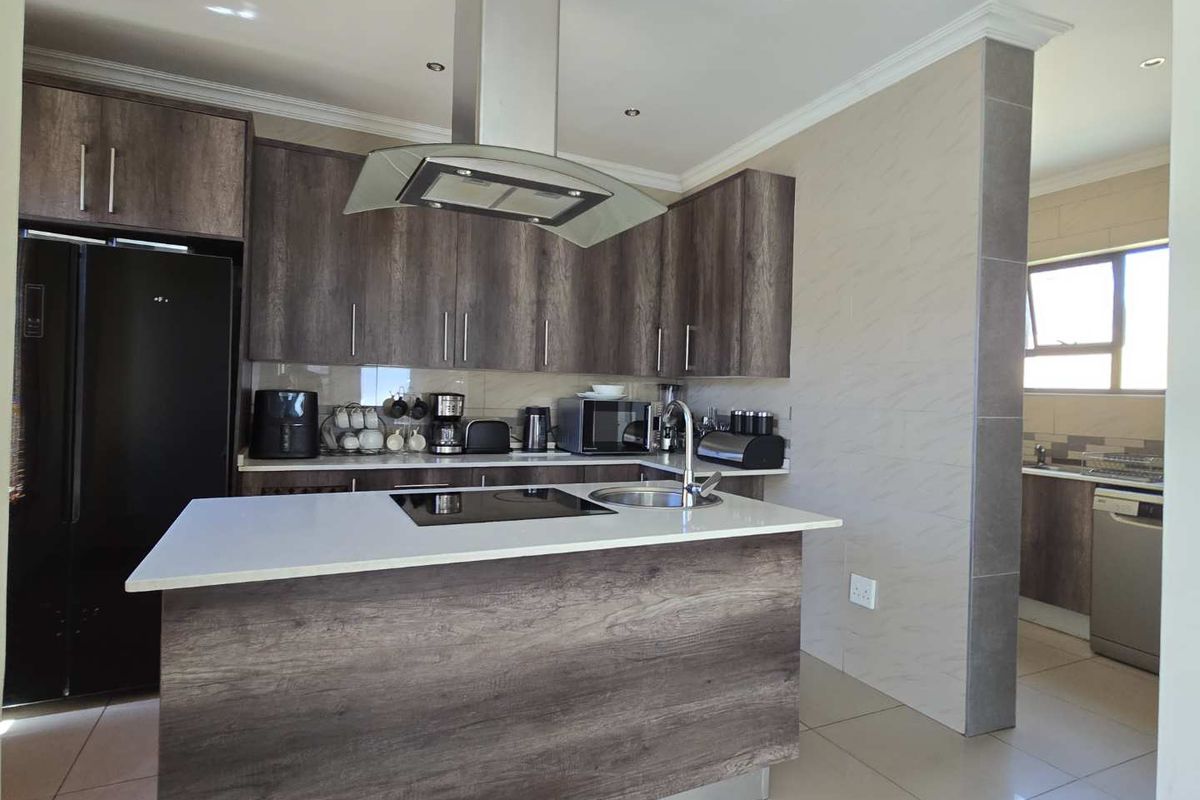 Modern kitchen featuring dark wood-grain cabinetry, a central island with a built-in hob and sink, stone countertops, and integrated extractor fan.