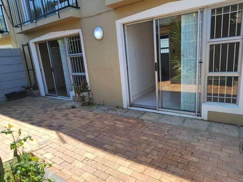 A paved ground-floor patio area featuring sliding glass doors with security bars, providing direct access to the apartment interior.