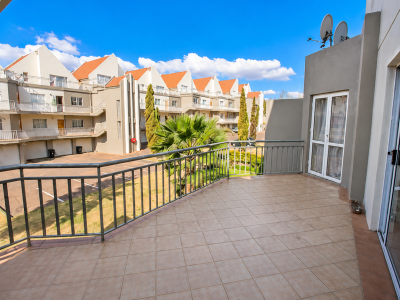 A spacious tiled balcony featuring a metal balustrade, offering an elevated view of the complex grounds and surrounding residential units.