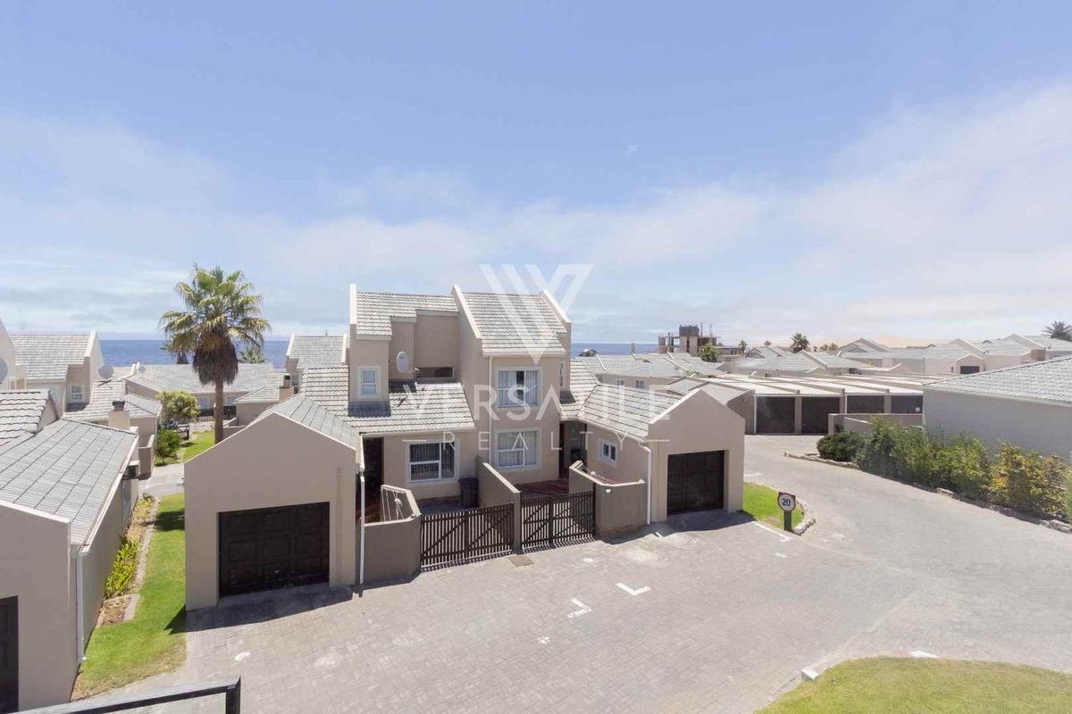 An elevated aerial view of a townhouse complex featuring paved driveways, tiled roofs, and private garage access within a coastal residential estate.