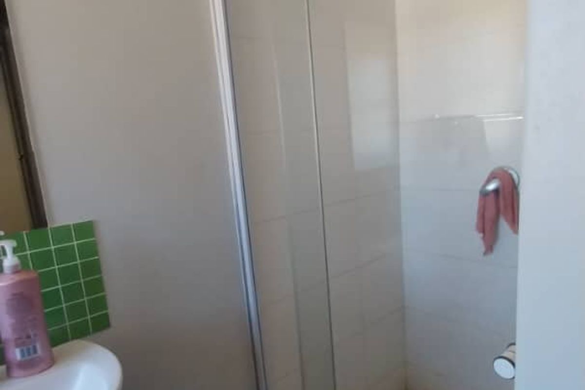 A functional bathroom featuring a glass-enclosed shower with white wall tiles and a wall-mounted basin with green tiled splashback.