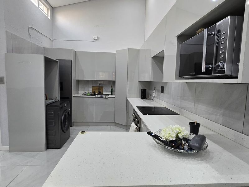 Modern kitchen featuring sleek grey cabinetry, quartz countertops, integrated appliances, and tiled flooring, with an adjacent view into the bathroom area.
