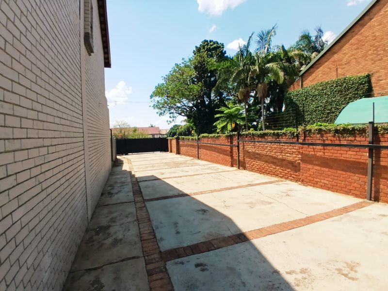 A paved driveway leading to a secure entrance gate, featuring brick boundary walls and established perimeter security fencing.