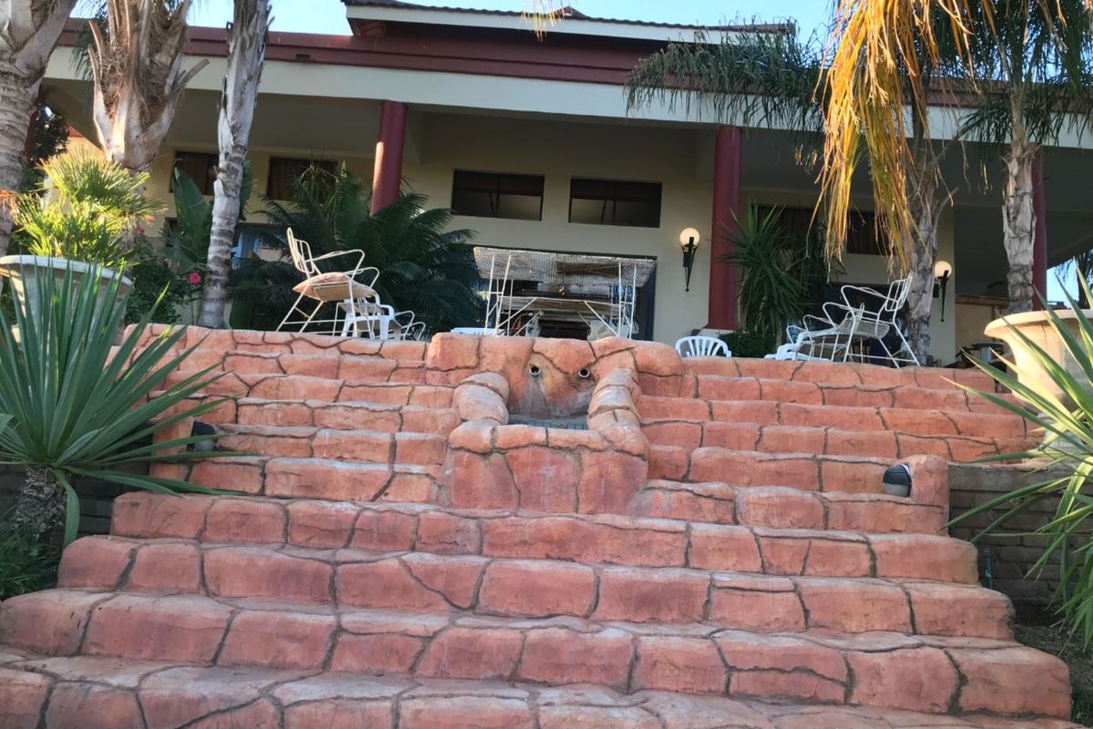 A rear exterior view featuring a covered patio area accessed by decorative stone-look stairs, set within a landscaped garden environment.