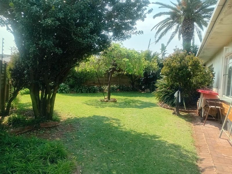 A spacious rear garden featuring a well-maintained lawn, mature trees, and a brick-paved pathway along the side of the house.