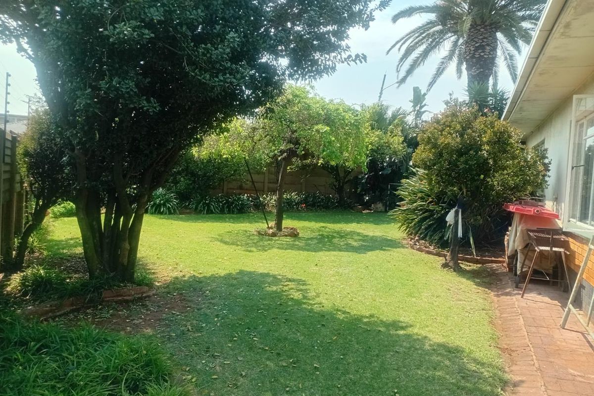 A spacious rear garden featuring a well-maintained lawn, mature trees, and a brick-paved pathway along the side of the house.