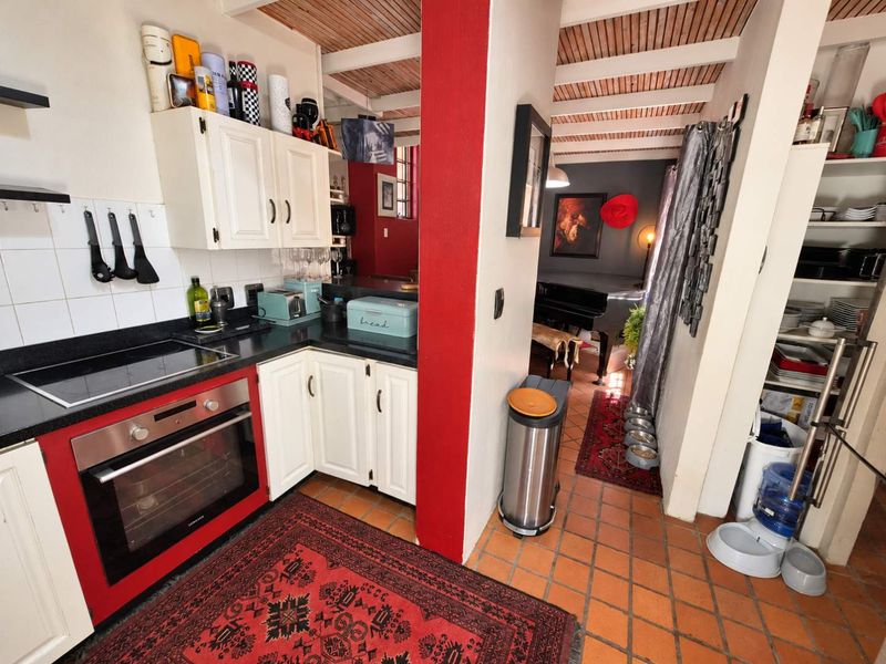A compact kitchen featuring built-in cabinetry, a tiled backsplash, an integrated oven and hob, and rustic exposed beam ceilings with terracotta floor tiles.