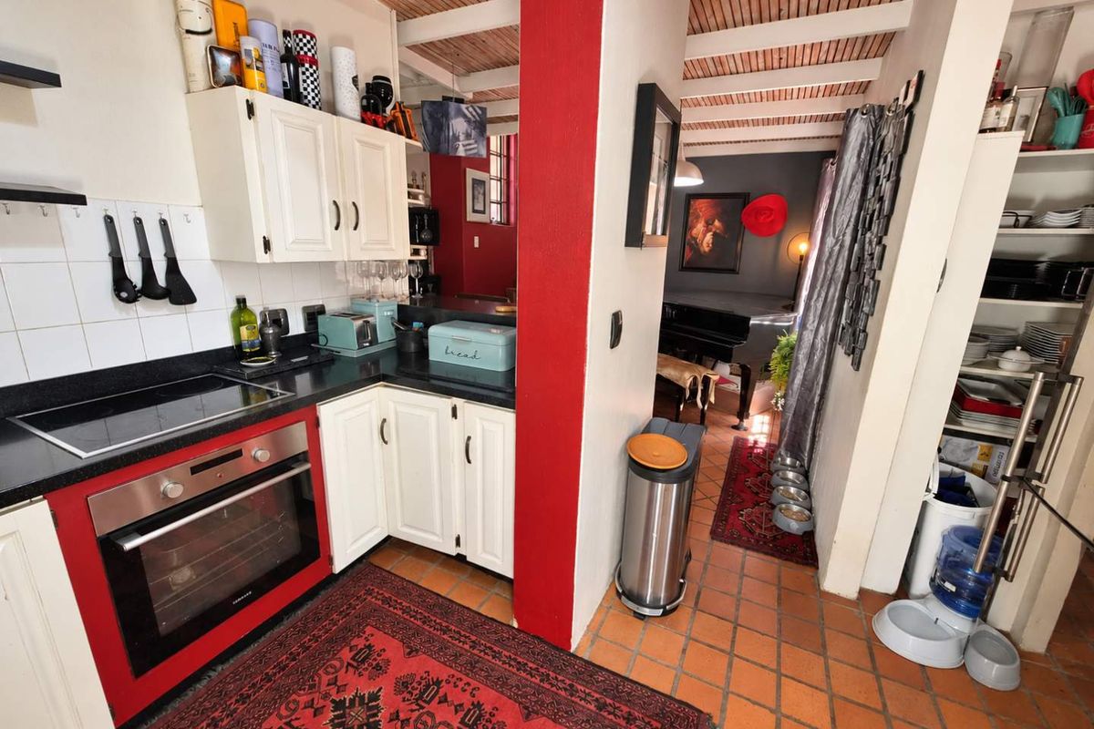 A compact kitchen featuring built-in cabinetry, a tiled backsplash, an integrated oven and hob, and rustic exposed beam ceilings with terracotta floor tiles.