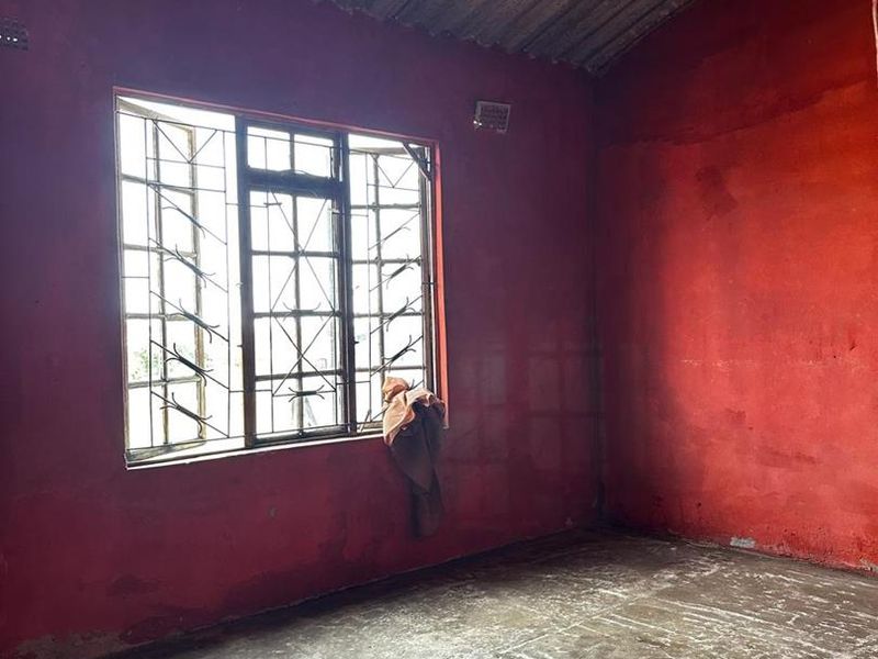 An empty room featuring exposed corrugated metal ceiling, concrete flooring, and security bars on the window, requiring significant renovation and finishing.
