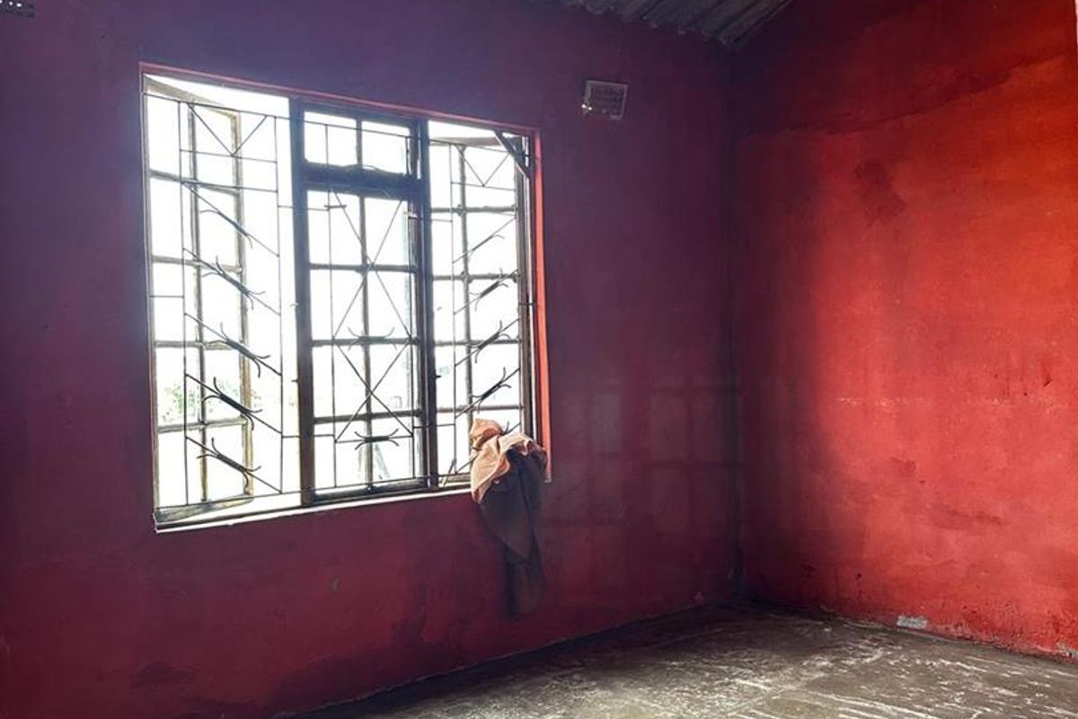 An empty room featuring exposed corrugated metal ceiling, concrete flooring, and security bars on the window, requiring significant renovation and finishing.