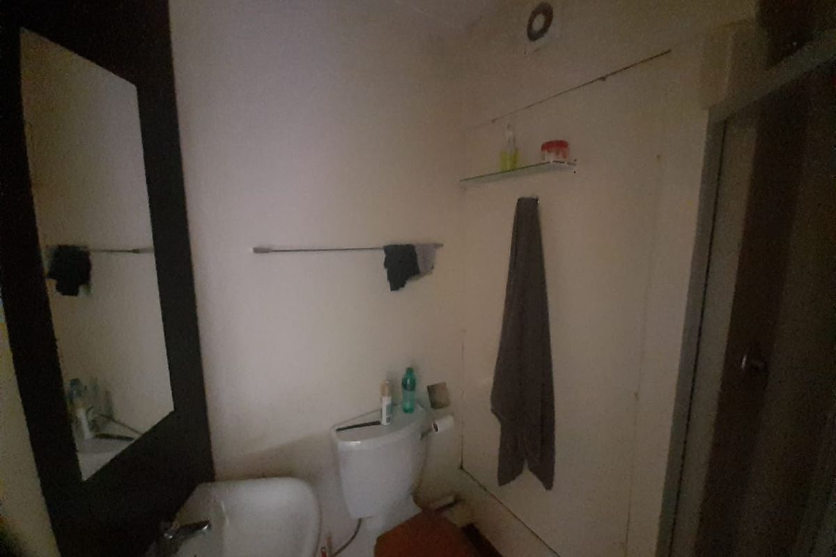 A compact bathroom featuring a standard washbasin, toilet, and extractor fan, requiring cosmetic updates to improve the overall aesthetic and lighting.