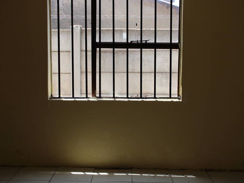 An empty room featuring tiled flooring and a window fitted with security bars, offering a blank canvas for potential interior updates.