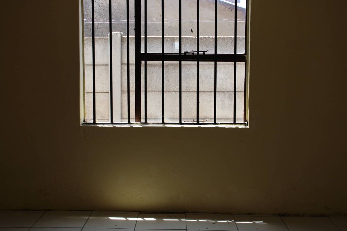 An empty room featuring tiled flooring and a window fitted with security bars, offering a blank canvas for potential interior updates.