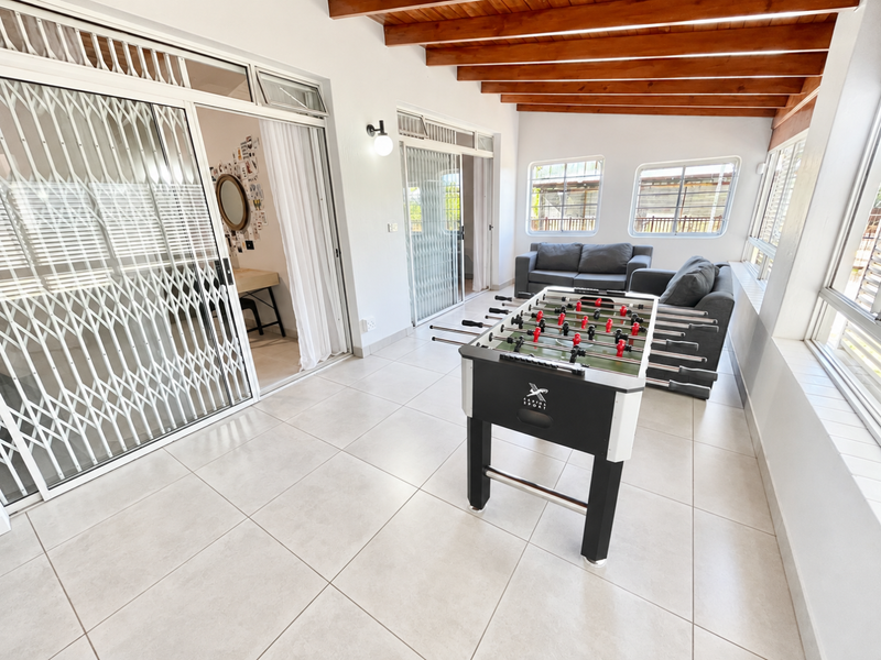 A bright, enclosed patio area featuring exposed timber ceiling beams, large format floor tiles, and sliding security gates leading to the interior.