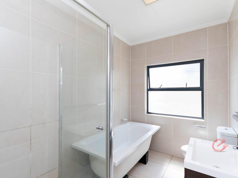 A clean, modern bathroom featuring a glass-enclosed shower, a freestanding bathtub, a vanity basin, and neutral wall tiling.