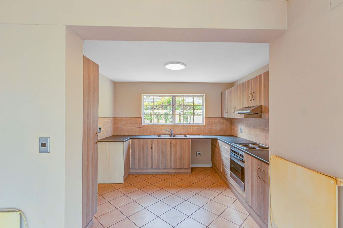 A functional kitchen featuring wood-look cabinetry, tiled splashbacks, a built-in oven with hob, and an extractor fan, finished with tiled flooring.