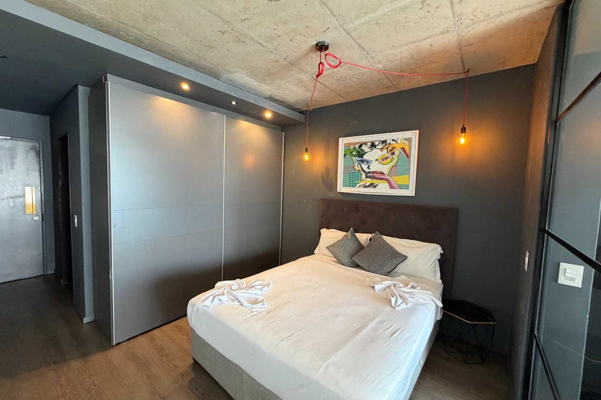 Modern bedroom featuring an exposed concrete ceiling, built-in sliding door wardrobe, and dark accent wall with industrial-style pendant lighting.