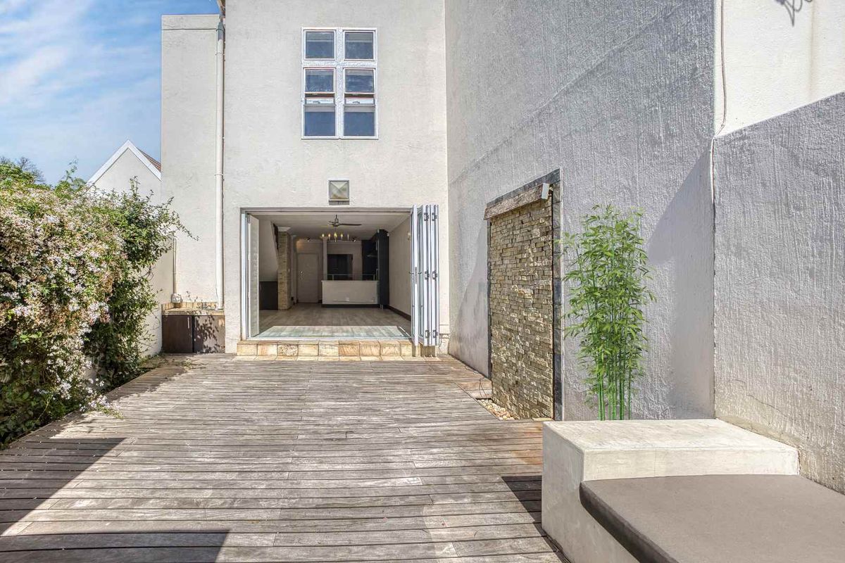 Rear exterior view featuring a timber deck, a stacked stone water feature, and bi-fold doors leading into the open-plan living area.