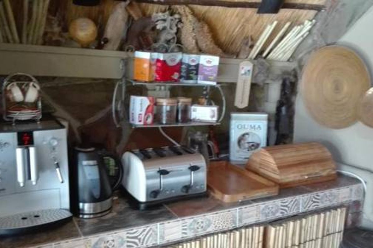 A rustic kitchen preparation area featuring tiled countertops, built-in shelving, and a thatched roof ceiling detail.