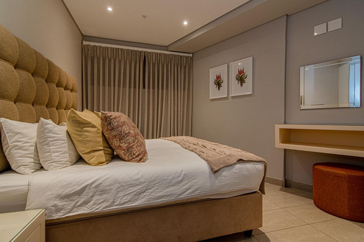 A well-maintained bedroom featuring neutral tones, recessed ceiling lighting, tiled flooring, and a built-in wall-mounted vanity unit.
