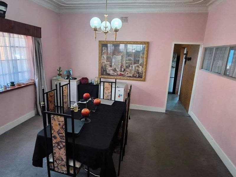 A dining room featuring ornate ceiling cornicing, a central chandelier, and pink wall finishes, providing a functional space for formal meals.