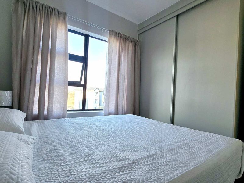 A well-maintained bedroom featuring a built-in sliding door wardrobe, neutral finishes, and natural light through an aluminium-framed window.