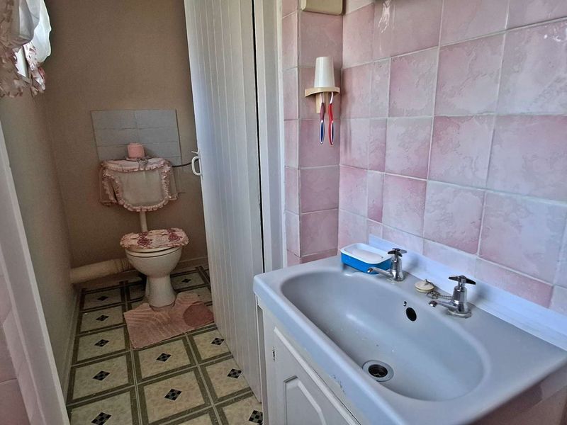 A dated bathroom featuring pink wall tiles, a standard toilet, and a pedestal washbasin with dual taps.