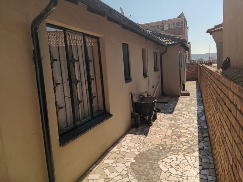 Rear exterior walkway featuring crazy paving, a brick boundary wall, and an external utility sink with security bars on the windows.