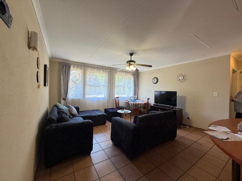 A functional living room featuring tiled flooring, a ceiling fan, and coved ceilings, providing a comfortable and well-lit space for relaxation.