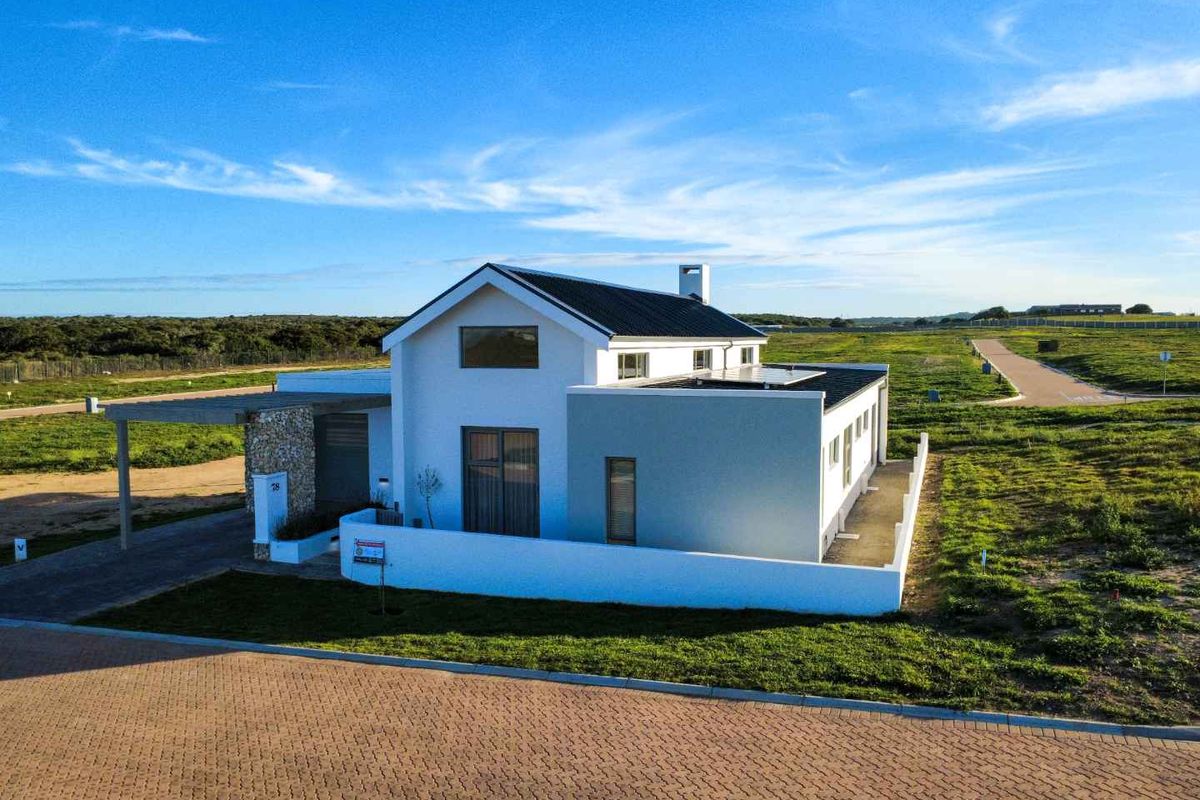 Aerial view of a modern detached house featuring a stone-clad entrance, paved driveway, and surrounding landscaped grounds in a quiet residential estate.