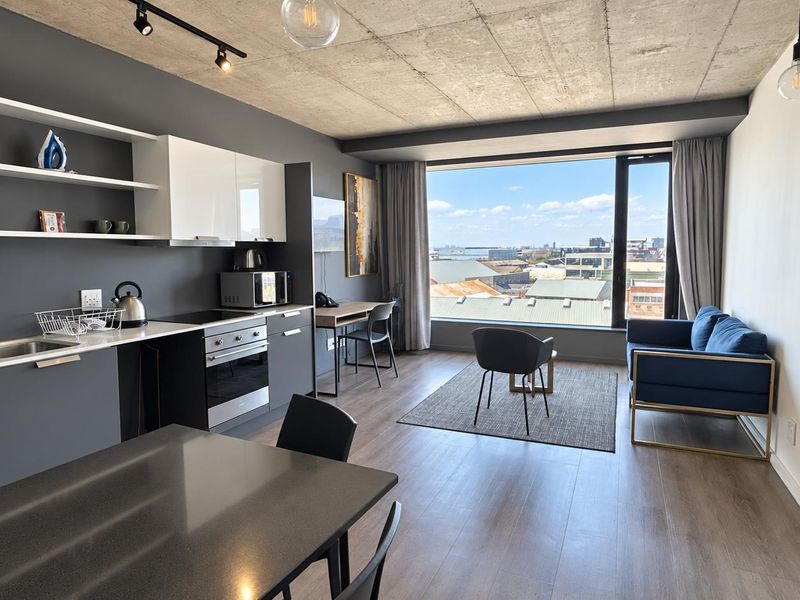 Modern open-plan apartment featuring an exposed concrete ceiling, sleek kitchen cabinetry, and a large window offering expansive city views.