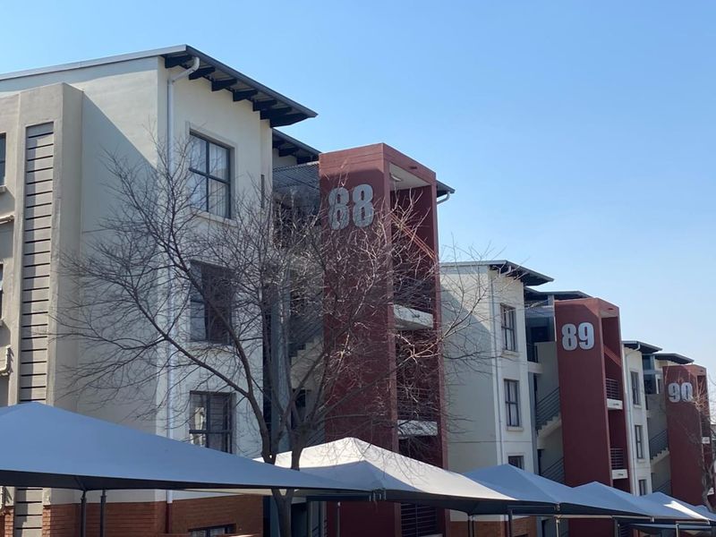 Exterior view of a modern multi-story apartment complex featuring numbered units, external stairwells, balconies, and covered parking bays.