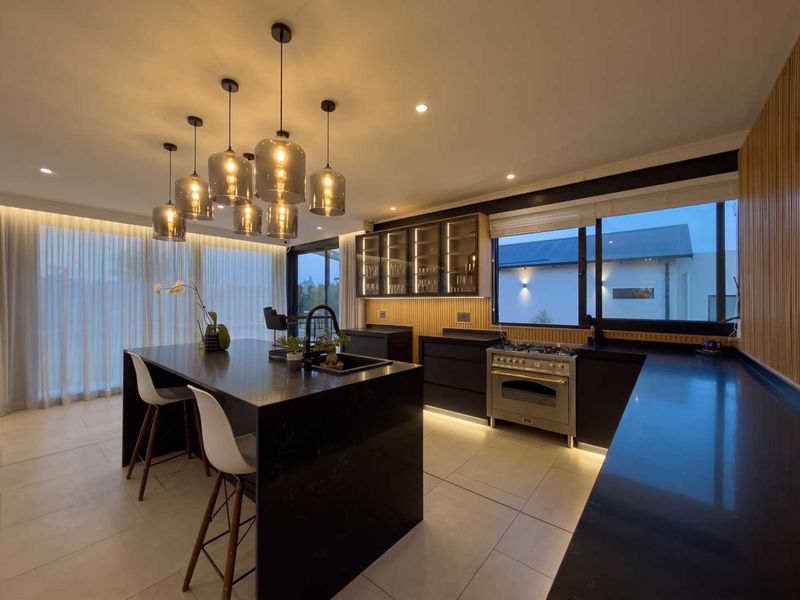 Modern kitchen featuring a large central island, high-end gas stove, sleek dark cabinetry, and elegant pendant lighting with integrated under-cabinet illumination.