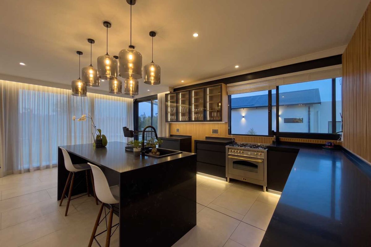 Modern kitchen featuring a large central island, high-end gas stove, sleek dark cabinetry, and elegant pendant lighting with integrated under-cabinet illumination.