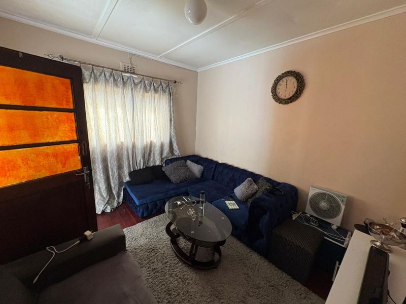 A cozy living room featuring hardwood flooring, a classic timber door, and a window with curtains, providing a comfortable and functional living space.