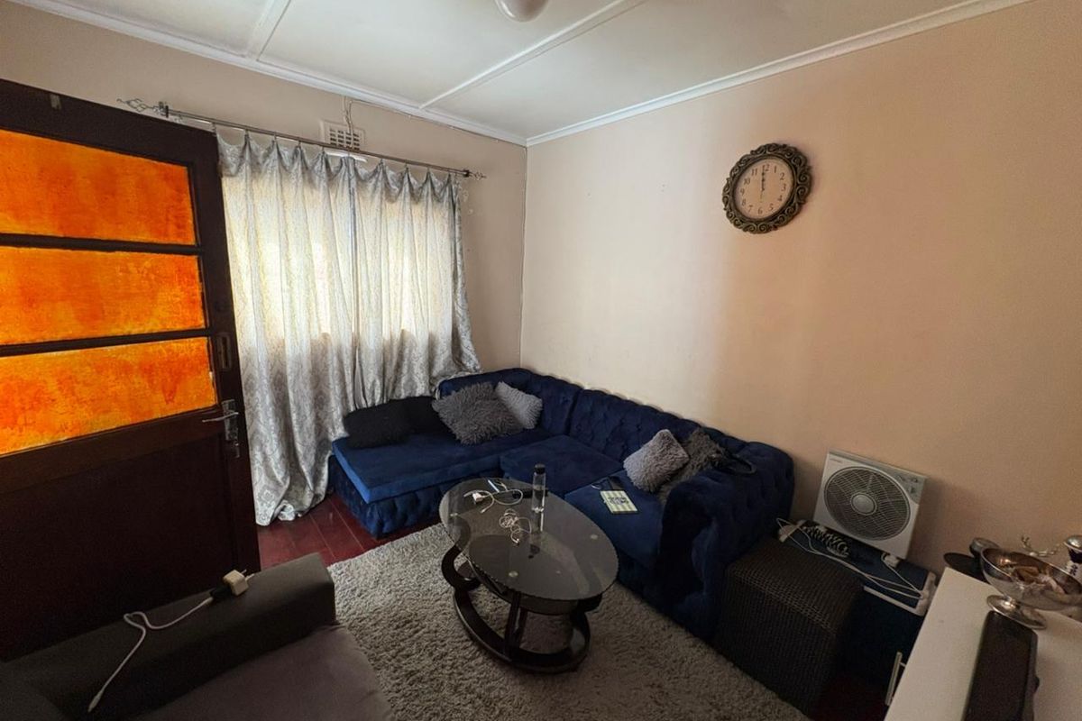 A cozy living room featuring hardwood flooring, a classic timber door, and a window with curtains, providing a comfortable and functional living space.